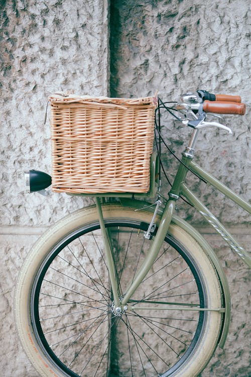 Retro bike with wicker basket standing next to white shabby uneven wall in city street in daytime