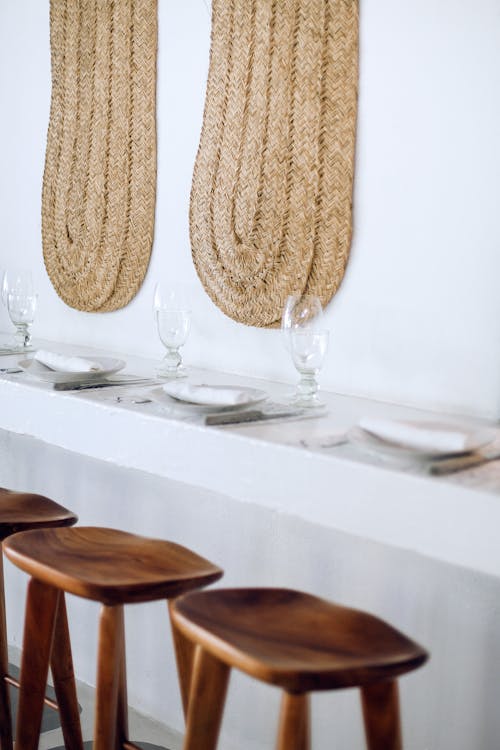 Creative design of table setting with glassware near stools and wall with wicker decor in cafeteria