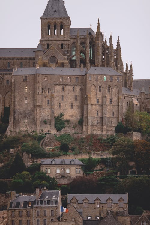 Free Facade of historic Mont Saint Michel Abbey with stone walls and spires built in Gothic style on island against cloudy evening sky Stock Photo
