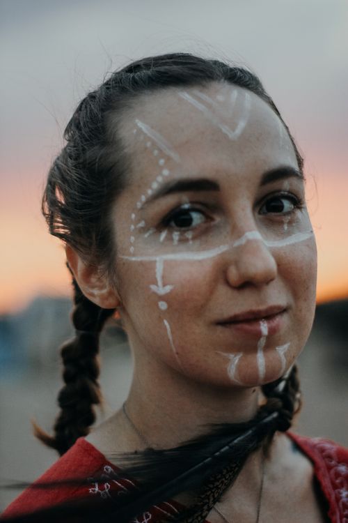 Free Close-up of a young woman with face paint and braided hair during sunset. Stock Photo