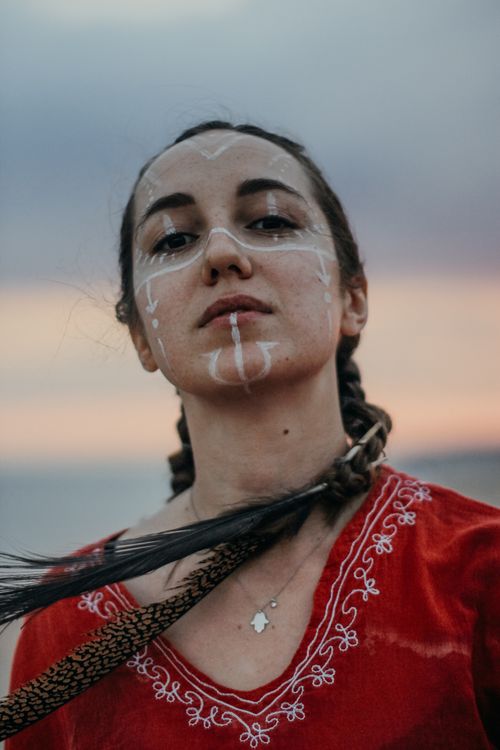 Free Close-up portrait of a woman with face paint and braids at sunset on a beach. Stock Photo