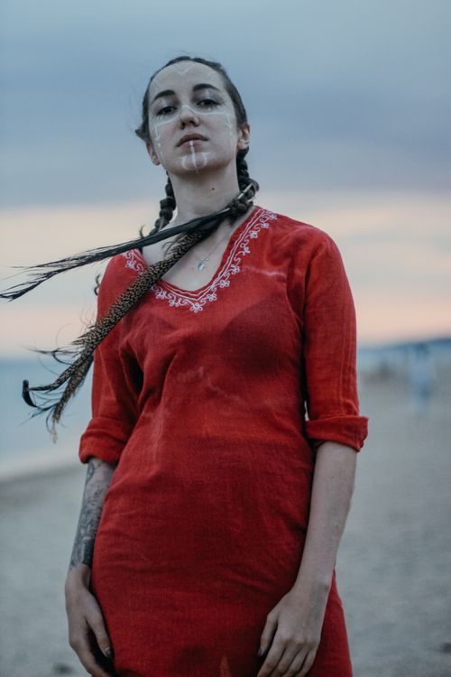 Free A young woman with braided hair and face paint standing confidently on a beach at twilight. Stock Photo