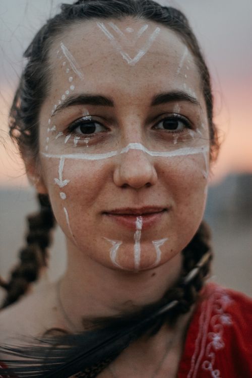 Free A close-up portrait of a woman with braided hair and tribal face paint outdoors. Stock Photo