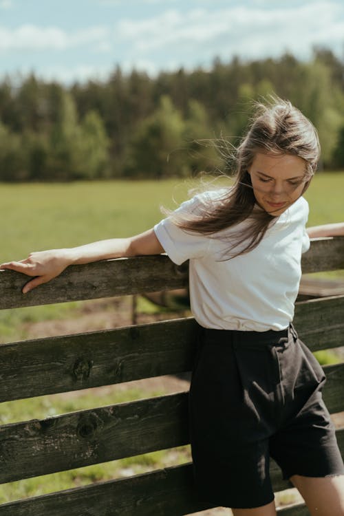 Girl in White Shirt and Black Skirt Standing on Brown Wooden Fence