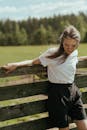 阳光明媚的乡村里，一名穿着休闲装的年轻女子靠在木栅栏上