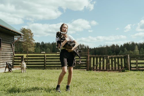 Free Woman in White Shirt and Black Shorts Carrying Black Backpack Standing on Green Grass Field during Stock Photo