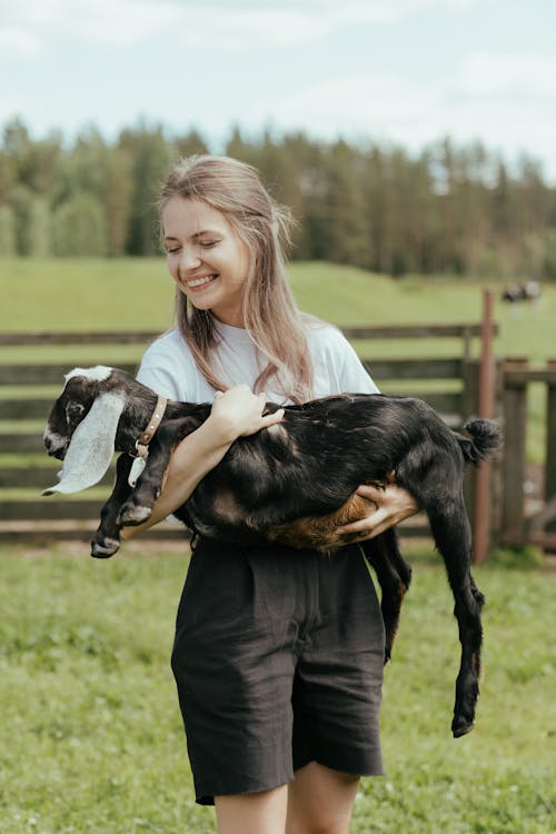 Woman in Black Jacket Holding Black and White Goat