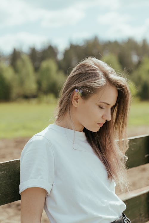 Woman in White Crew Neck Shirt Sitting on Brown Wooden Bench