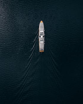 Drone shot capturing a lone ship navigating tranquil waters with ripples trailing behind.