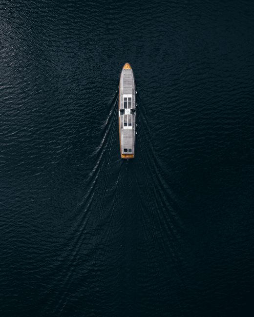 Drone shot capturing a lone ship navigating tranquil waters with ripples trailing behind.
