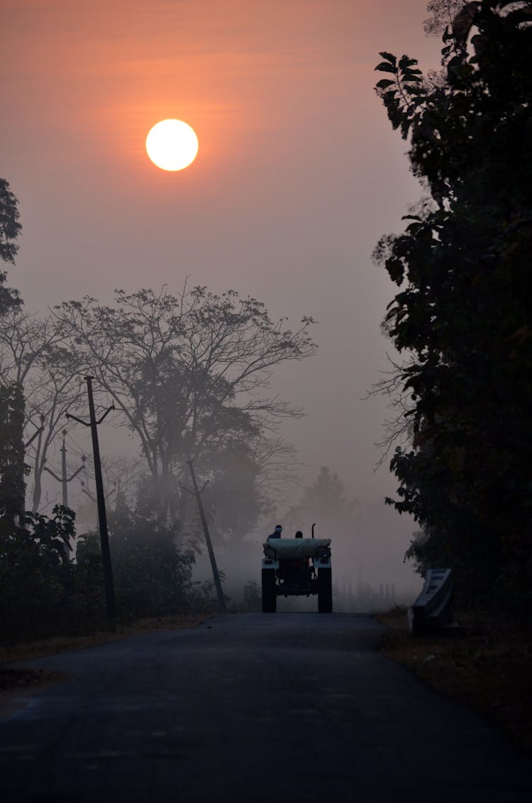 A Bright Sun Over People Riding A Tractor On The Road