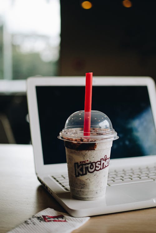 Free Sugary drink in big transparent disposable cup with red straw on white laptop on table on blurred background Stock Photo