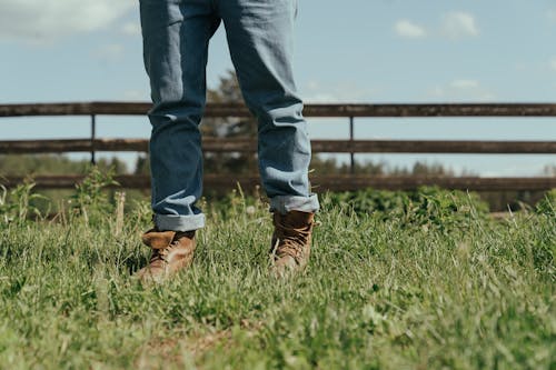 Person in Blue Denim Jeans and Brown Leather Boots Standing on Green Grass Field