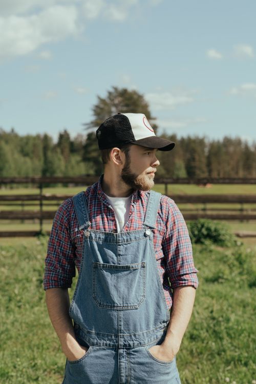 Free Bearded male farmer in denim overalls standing on a sunny day in a rural setting. Stock Photo