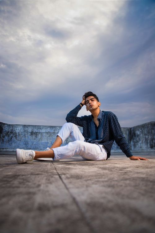 Free Stylish young man sitting on urban rooftop under cloudy sky in Surat, India. Stock Photo