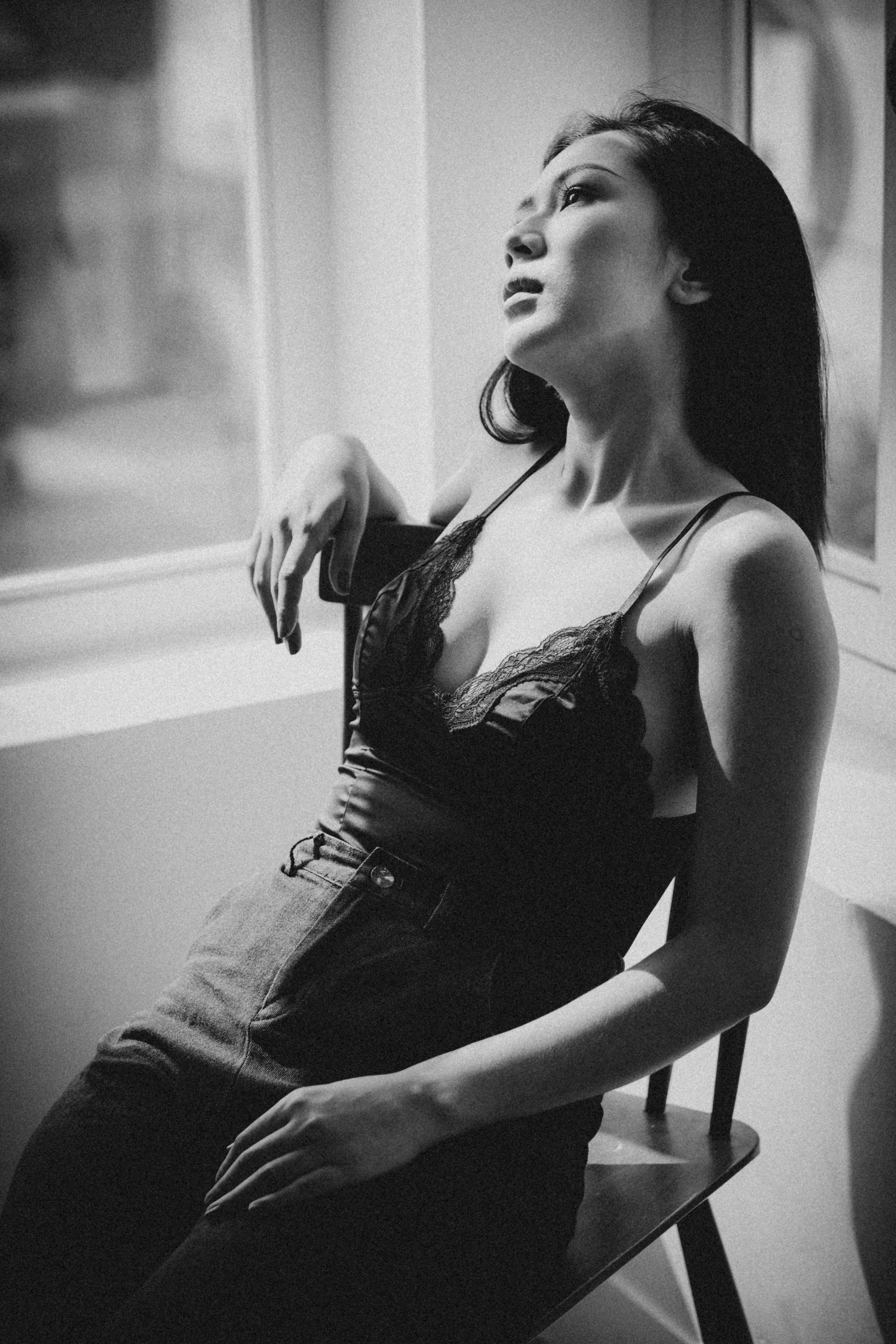 Free A serene black and white portrait of a young woman sitting by a window, exuding elegance and contemplation. Stock Photo