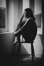 一个女人若有所思地坐在窗前的椅子上，营造出一种宁静的氛围
