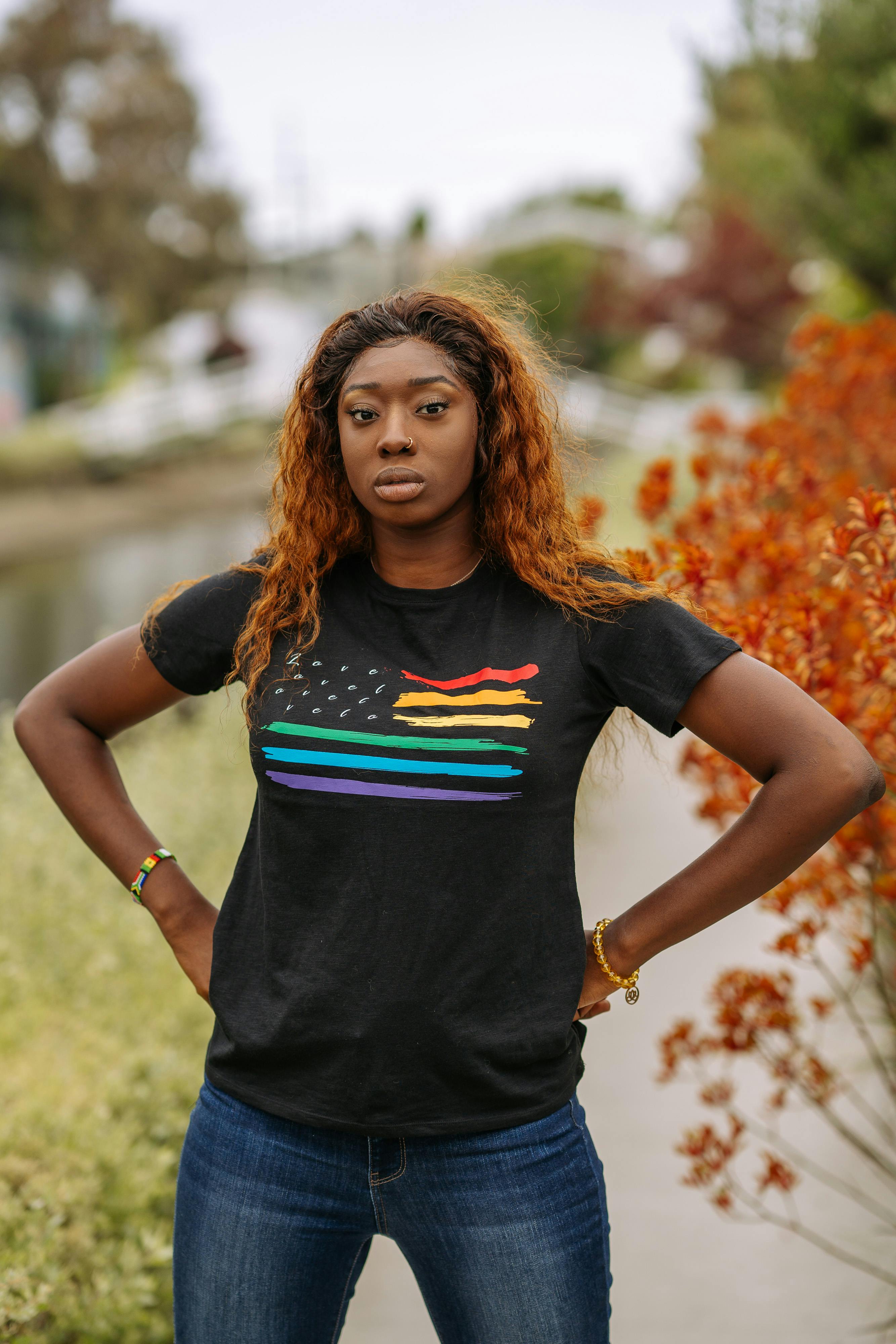 一位身穿彩虹旗衬衫的女子在户外自信地摆出姿势，展现了骄傲与力量