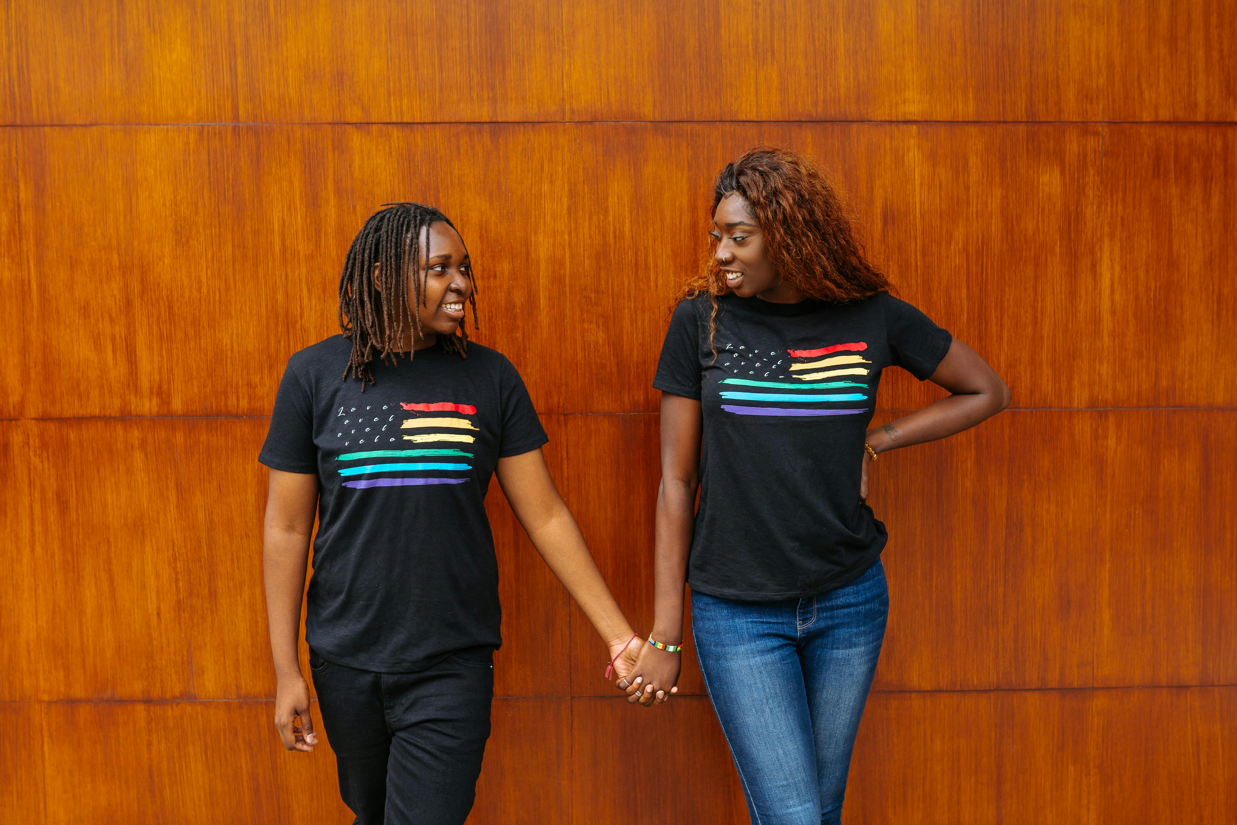 2 women in black t shirt standing beside brown wooden wall