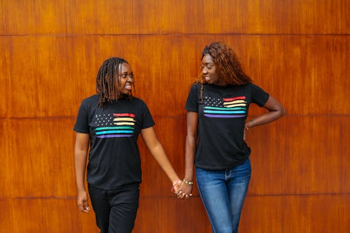 2 Vrouwen In Zwart T Shirt Staan Naast Bruine Houten Muur