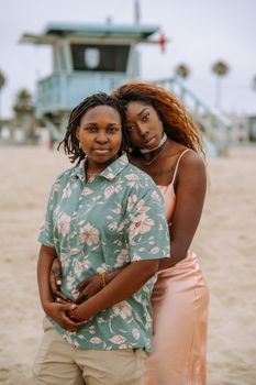 A loving couple embraces on the beach near a lifeguard tower, exuding warmth and connection.
