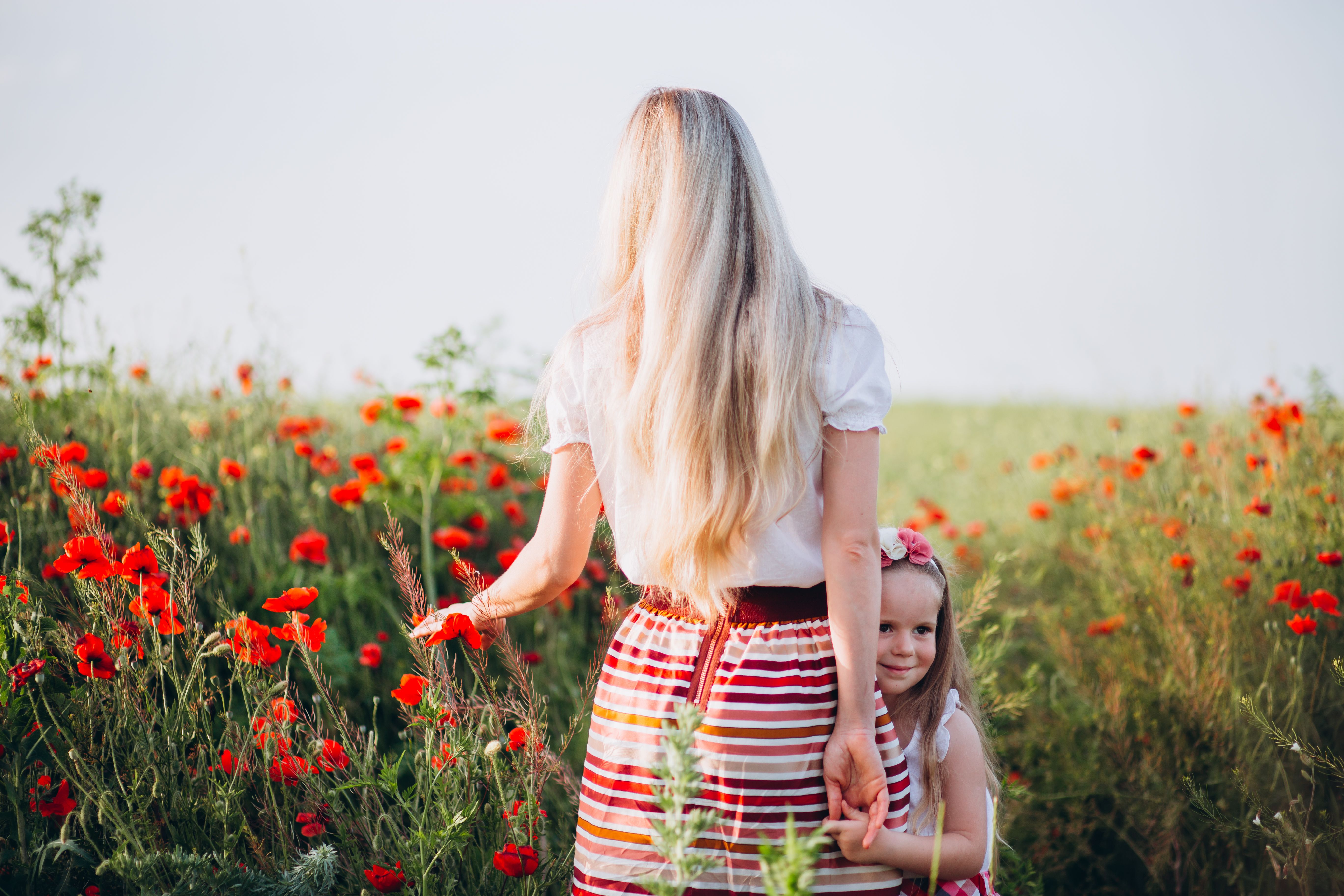 Cheerful girl holding hand of faceless mother in field · Free Stock Photo