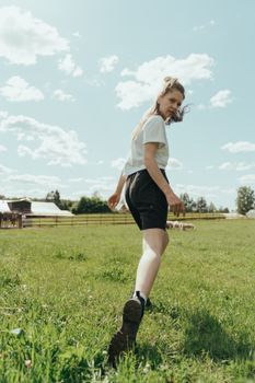 A young woman walks through a lush green field, enjoying the rural landscape on a sunny day.