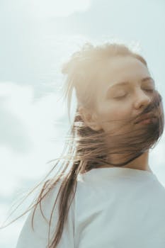 一幅梦幻般的户外肖像画中，一位闭着眼睛、头发随风飘扬的女人被描绘出来