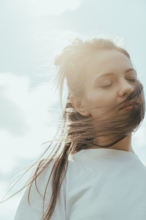 Free A dreamy outdoor portrait of a woman with eyes closed and hair blowing in the wind. Stock Photo