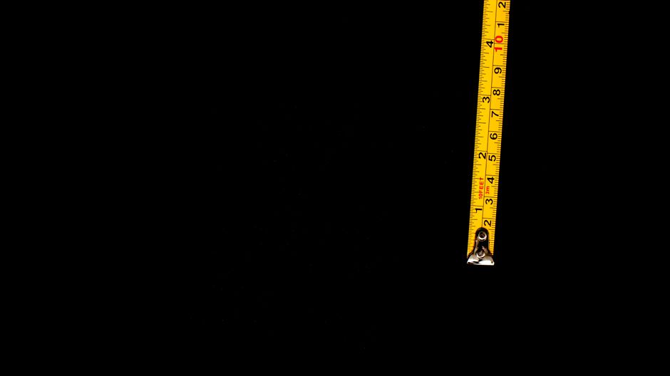 Close-up of a yellow measuring tape against a black background, ideal for design projects.