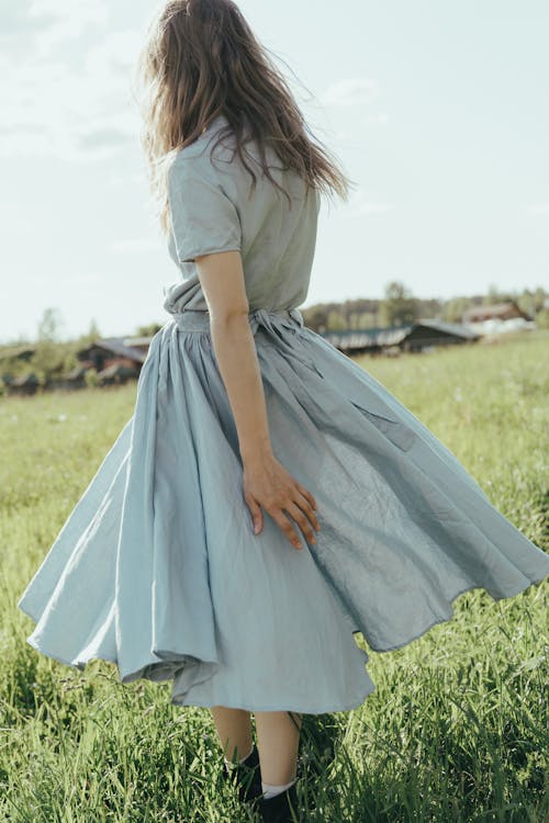 Woman in White and Blue Dress Standing on Green Grass Field