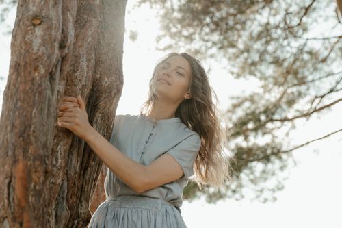 Free A serene woman enjoying nature with sunlit trees in the background, evoking tranquility. Stock Photo