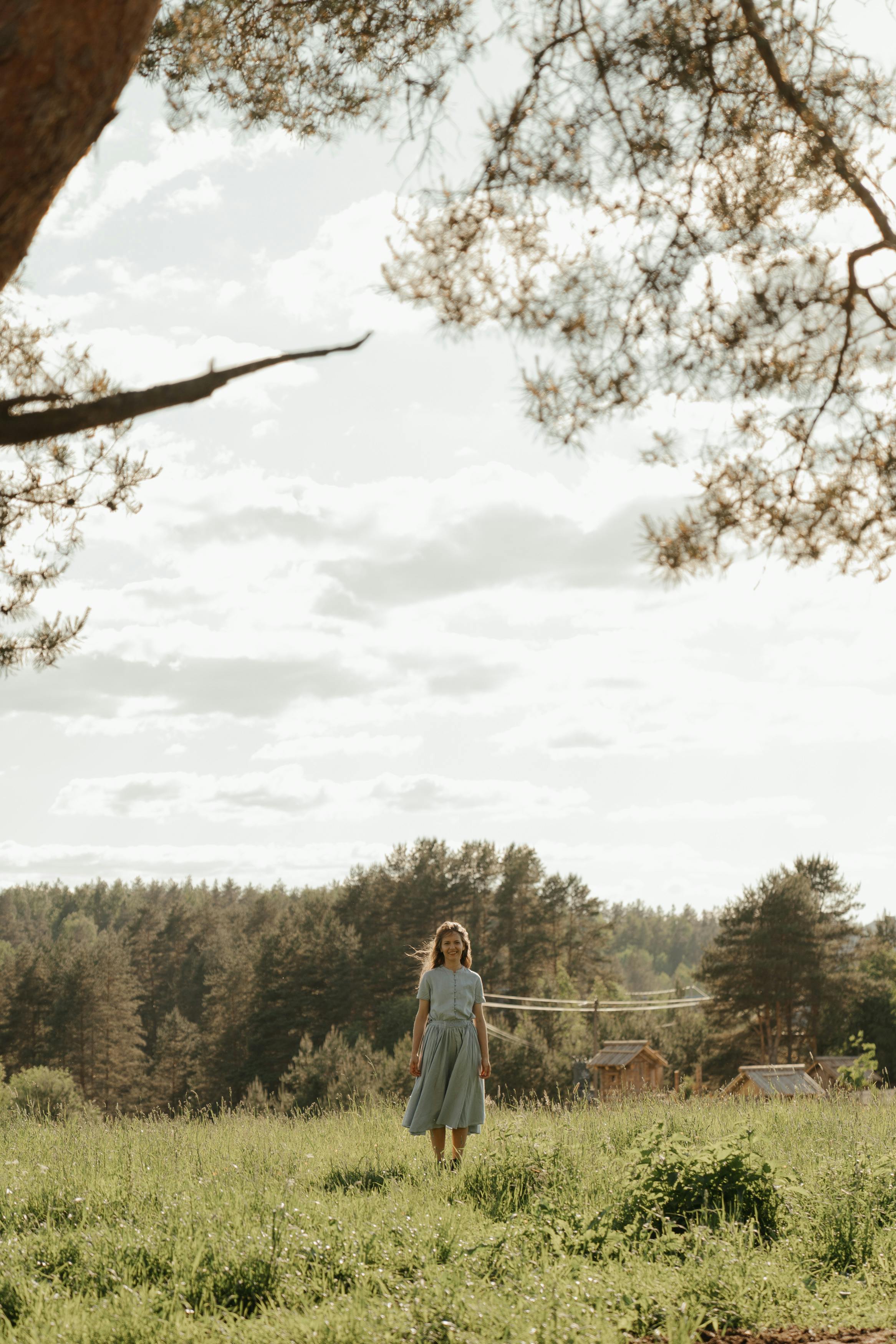 一位身着夏装的女人，在明亮的天空下走过郁郁葱葱的草地