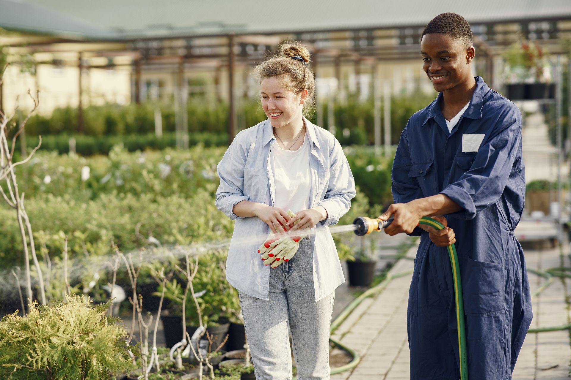 Young gardeners collaborating to water plants in a lush greenhouse setting.