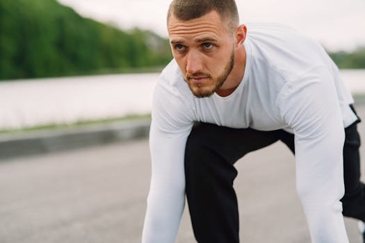 Athletic man in sportswear on a starting line, ready for a sprint workout outdoors.