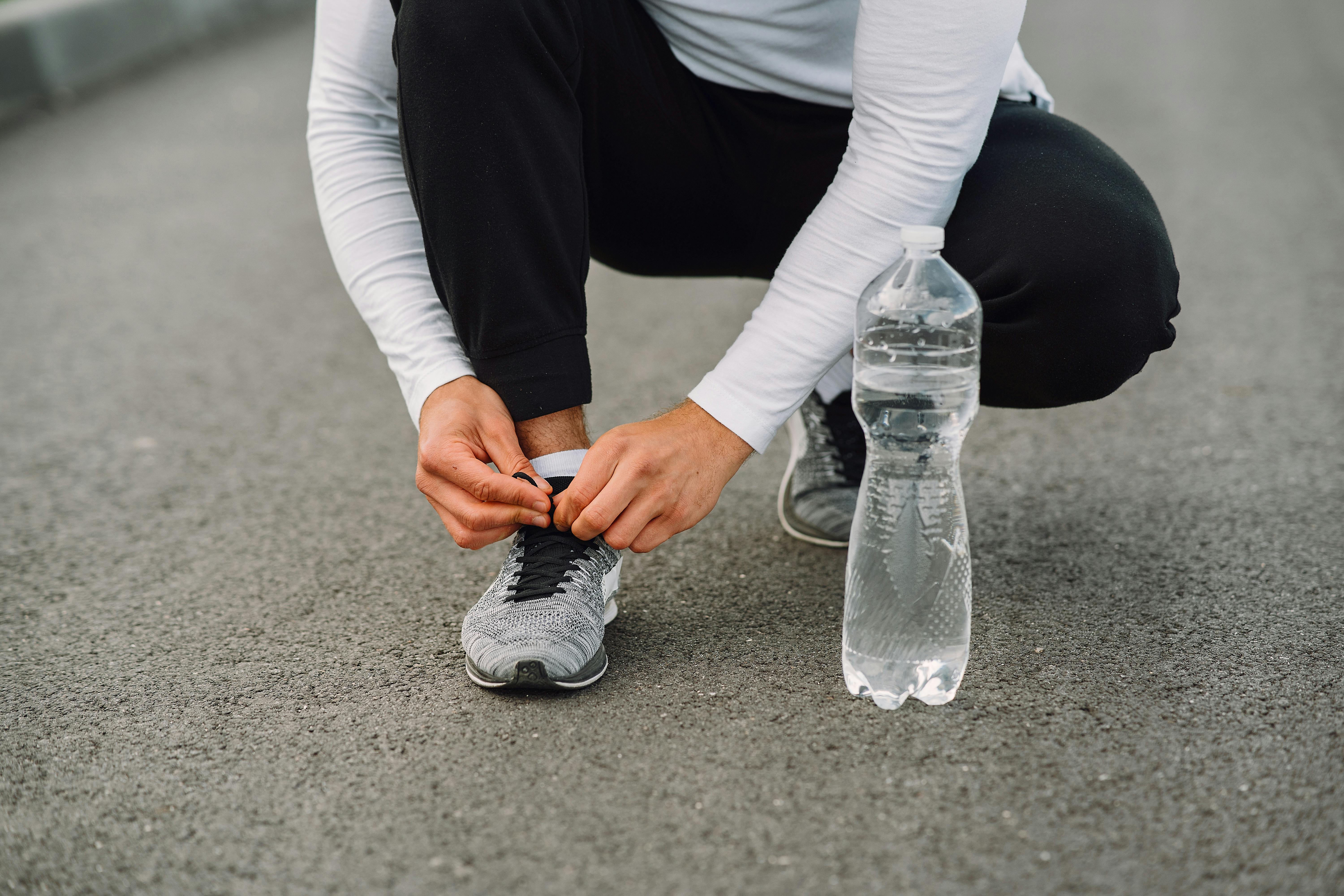 Runner tying shoelaces on the road with a water bottle beside. Fitness preparation. - best morning exercises