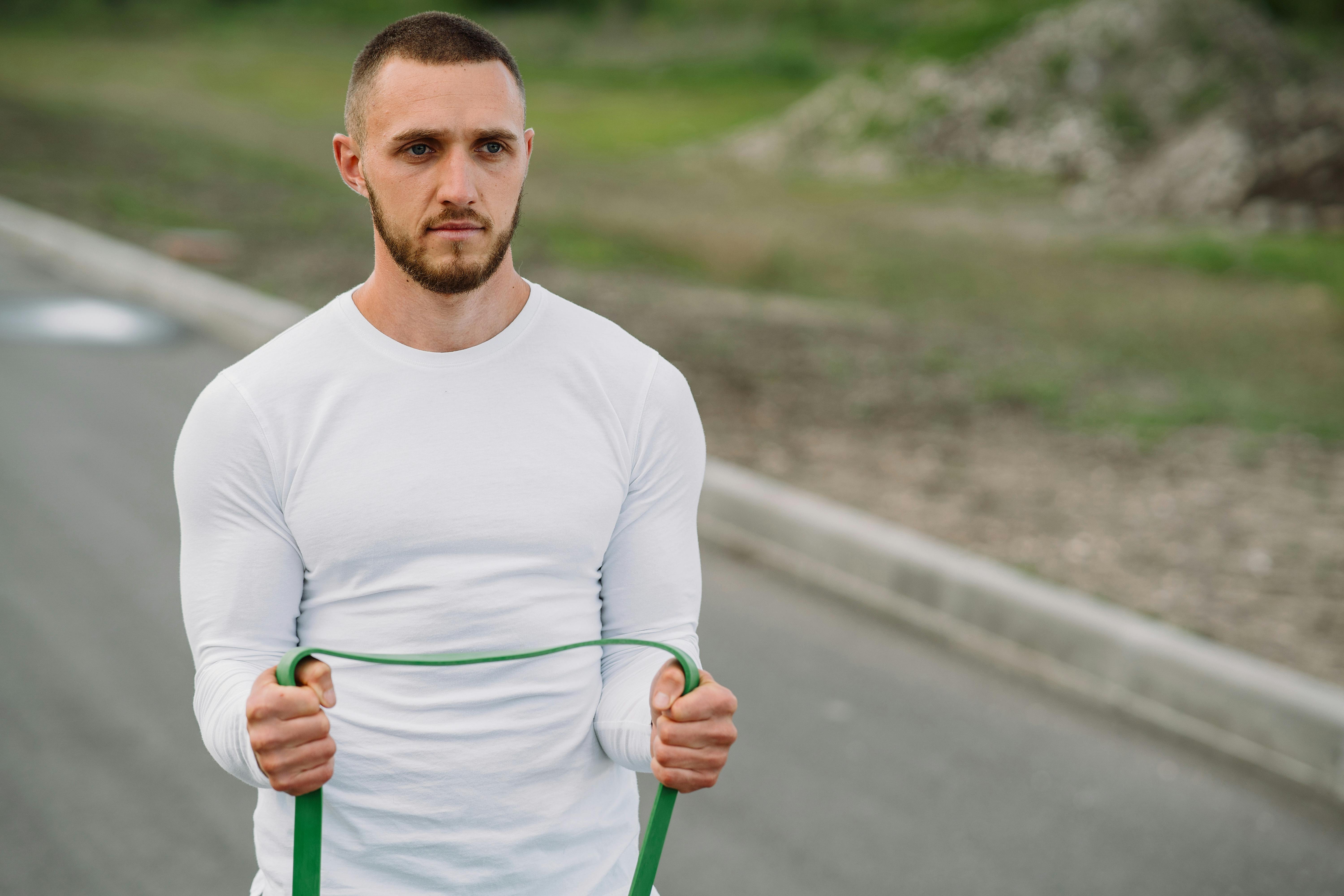 Adult man working out with a resistance band on an outdoor road.