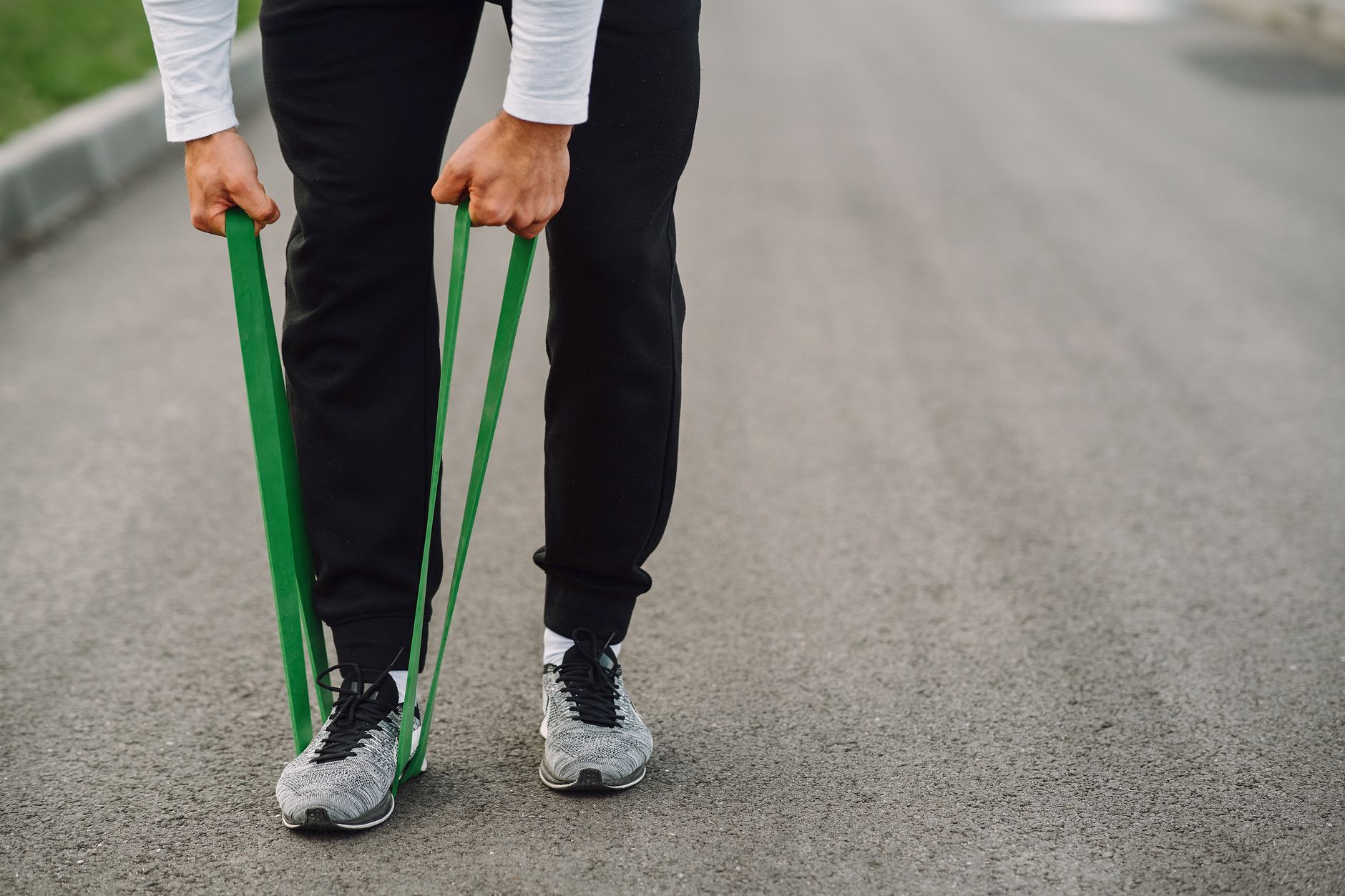 An athlete uses green resistance bands for a workout on a paved path.