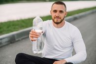 Athletic man with bottled water sitting outdoors, promoting hydration.