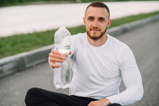 Athletic man with bottled water sitting outdoors, promoting hydration.