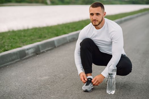 A man in athletic wear ties his shoe on a road, ready for exercise.