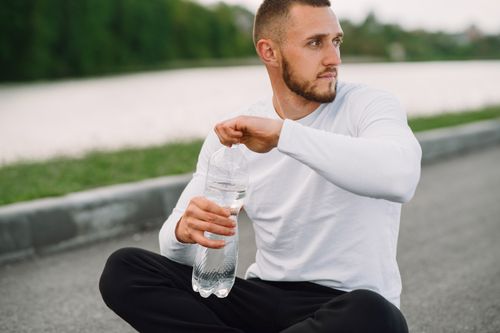 Free Young man in sportswear enjoying a break outdoors with a water bottle, promoting a healthy lifestyle. Stock Photo