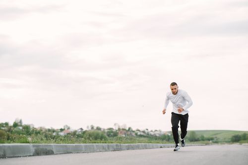 Free A man in sportswear jogging on a road, showcasing outdoor fitness. Stock Photo