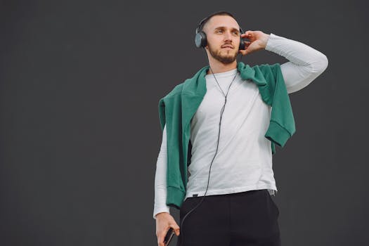 A stylish man enjoys music with headphones, outdoors. Casual style with green sweater and white shirt.