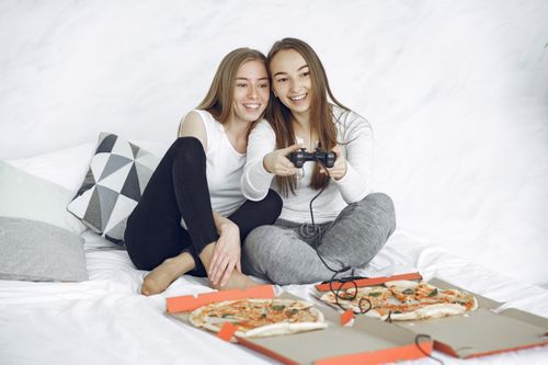 Free Two young women enjoy a fun gaming session with delicious pizza in a cozy setting. Stock Photo