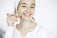 一位年轻女子在室内微笑着用刷子化妆