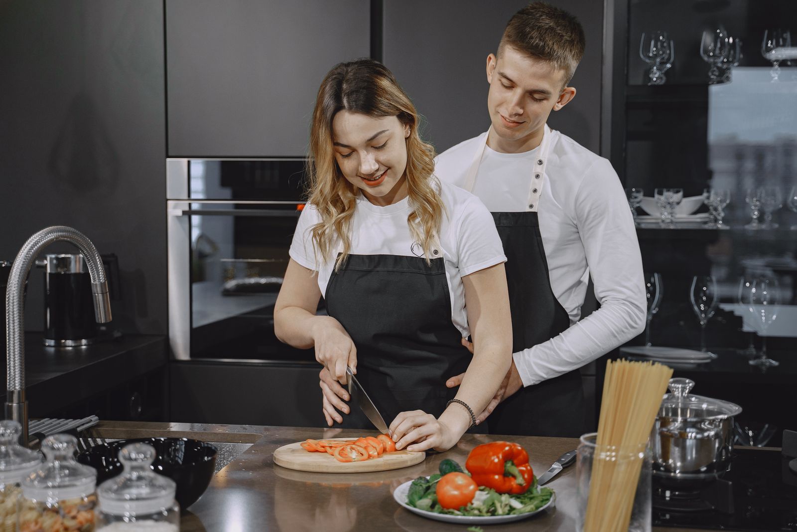 Happy couple wearing aprons cutting vegetables together on a kitchen counter.