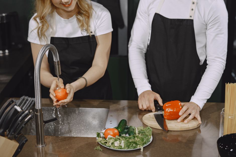 Two adults wash and slice fresh vegetables on a kitchen counter.