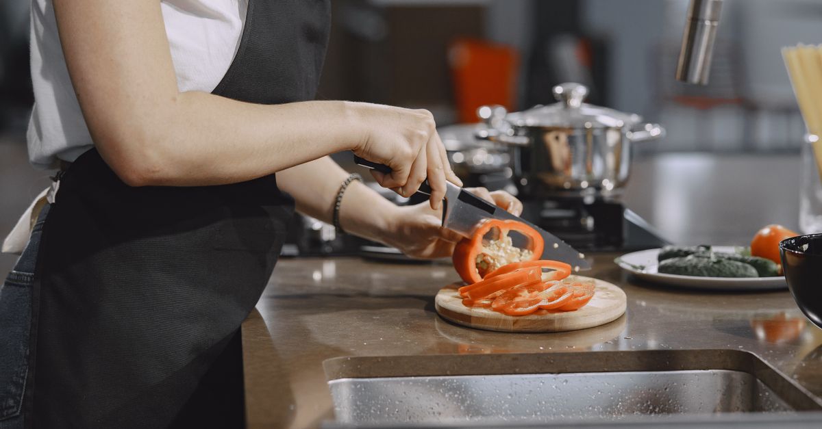 Woman slicing tomatoes in a modern kitchen setting with cooking equipment on the counter.