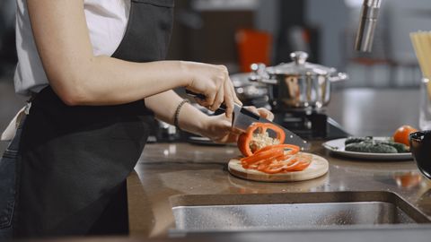 Woman slicing tomatoes in a modern kitchen setting with cooking equipment on the counter.